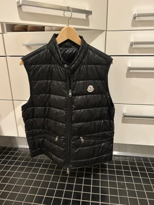 Moncler Gui väst - Svart väst från moncler. Storlek 3 (M). Nypris är ca. 6000kr, mitt pris är 2500kr. Den är i mycket bra skick, sparsamt använd. QR-kod funkar. 
