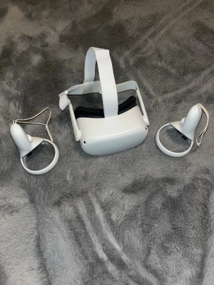 Oculus Quest 2 VR-headset med kontroller - Säljer ett Oculus Quest 2 VR-headset i vitt med tillhörande två handkontroller. Headsetet har justerbart huvudband i tyg och mjuk vaddering runt ögonen för extra komfort. Perfekt för dig som vill uppleva VR-spel och appar på riktigt. Det är inget fel på den alls. Funkar hur fint som helst!