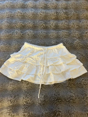 Vit volangkjol från Gina Tricot - Supersöt vit kjol från Gina Tricot med flera volanger och knytband i midjan. Kjolen är i storlek xs och använd ca 3 gånger❤️