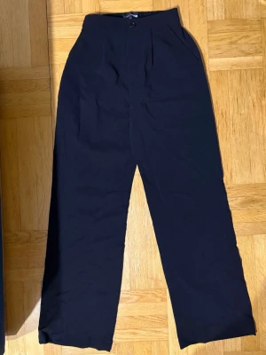 Svarta vida kostymbyxor hög midja - Säljer ett par svarta kostymbyxor med hög midja och vida ben. Byxorna har en klassisk knappstängning framtill och sidofickor. Perfekta för en clean och stilren look, passar till skjorta eller crop top. Materialet känns mjukt och följsamt.