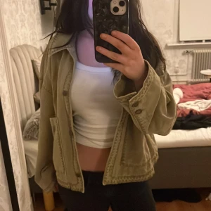 Olivgrön vår jacka från Zara - Säljer en olivgrön jacka från Zara i bomull. Jackan har två stora fickor framtill, knappar vid ärmslut och en avslappnad passform. Perfekt att slänga över en t-shirt för en chill look.