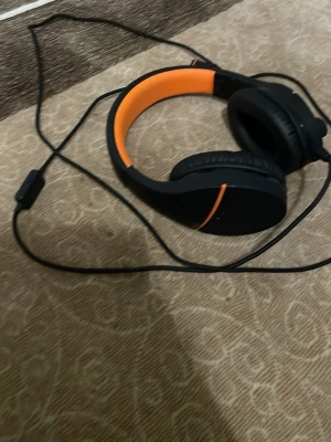Kabelanslutna over-ear hörlurar, svart/orange - Bekväma over-ear hörlurar med kabelanslutning och mikrofon på sladden. Snygg svart design med orange insida. Passar perfekt för musik, spel eller videosamtal. Inga synliga defekter eller större slitage, ser ut att vara i gott skick.
