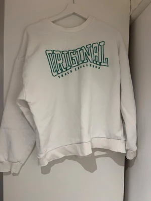 Vit sweatshirt med grön text - Säljer en vit sweatshirt med trycket 'ORIGINAL' i grön text på bröstet. Tröjan har rund halsringning och långa ärmar. Perfekt för en avslappnad och sportig stil.