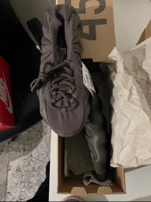 Adidas Yeezy 450 mörkgrå sneakers - Unika Adidas Yeezy 450 sneakers i mörkgrå färg med futuristisk design och vågig sula. Ovandelen är i stickad textil med snörning för skön passform. Perfekta för dig som vill sticka ut med en modern och trendig look.