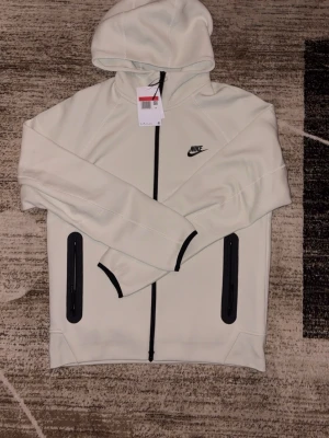 Nike tech fleece - Etiektt finns kvar. Skulle inte kalla denna färg för vit. Mer ljus grön/vit
