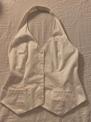 Vit korsettopp - Säljer en super snygg vit korsettopp från Zoul i storlek 42. Halterneck och justerbart band med spänne bak. Snygg v-ringning och figurnära passform.