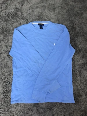 Ljusblå långärmad tröja Polo Ralph Lauren - Ljusblå långärmad tröja från Polo Ralph Lauren i 100% bomull. Klassisk rund halsringning och diskret broderad logga på bröstet. Perfekt för en avslappnad men ändå stilren look.