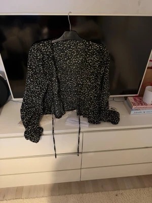 Svart blus med vita blommor  och knytband - Trendig svart blus med vita blommor och långa ärmar. Blusen har knytband framtill och en lös, luftig passform. Perfekt till jeans eller kjol för en cool och avslappnad look. Materialet känns lätt och flowy, vilket gör den skön att bära hela dagen en varm sommardag. Köpt på SHEIN ordpris 100kr säljer för 50kr plus frakt