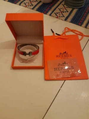 Rött Hermès armband i läder - Snyggt rött armband från Hermès i läder med silverfärgat H-spänne. Kommer i original ask och påse, perfekt för dig som gillar exklusiva accessoarer med ikonisk design. Armbandet har en stilren och modern look som sticker ut.