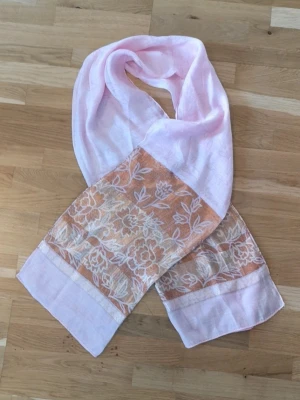 Ljusrosa sjal med blommigt mönster - En tunn och mjuk ljusrosa sjal med breda kanter i beige och vitt blommönster.