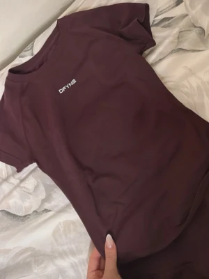 Topp DFYNE - Kortärmad vinröd topp från DFYNE med vit loggavitt framtill och baktill vid nacken. Väldigt stretchig och passar perfekt för gymmet! 🤎 (Espresso)