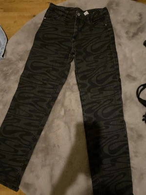 Svarta jeans med vågmönster -  Svarta jeans med grått vågmönster över hela byxan. Tillverkade i mjukt bomullsjeansmaterial. Finns inga defekter.