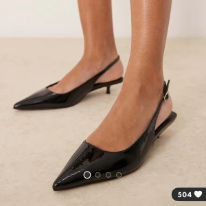 Svarta lackade pumps med spetsig tå - Snygga svarta pumps från New Look med glansig lackad yta och spetsig tå. Skorna har låg klack och öppen häl med justerbar rem. Perfekta för dig som gillar stilrena och trendiga detaljer. Materialet är syntet och designen är elegant med en modern touch. Andvända endast en gång och i väldigt bra skick. 