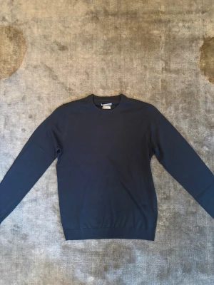 Mörkblå merinotröja These Glory Days - Snygg mörkblå rundhalsad tröja från These Glory Days i mjuk och tunn merinoull. Helt ny och oanvänd, nypris 800kr men säljer för 399kr. Klassisk modell med lång ärm och ribbade muddar vid hals, ärmslut och nederkant. Perfekt för dig som gillar stilrena och tidlösa plagg.
