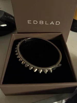 Silvrigt nitat armband från Edblad - Coolt armband i silverfärgad metall från Edblad med nitar runt hela bandet. Armbandet är stelt och har en modern, edgy design som sticker ut. Perfekt accessoar för dig som gillar att addera lite attityd till din stil.