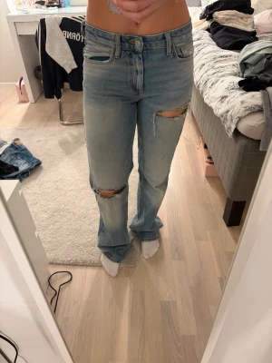 Ljusblå slitna jeans med raka ben - Säljer ett par ljusblå jeans med raka ben och slitna detaljer vid knäna. Jeansen har klassisk femficksdesign och normal passform. Perfekta för en avslappnad och trendig look.