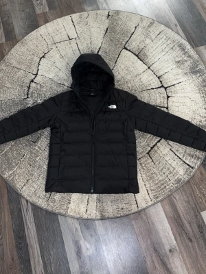 Svart dunjacka från The North Face - Snygg svart dunjacka från The North Face med huva och dragkedja framtill. Jackan har quiltad design och är perfekt för kalla dagar. Klassisk logga på bröstet och långärmad modell som håller dig varm hela vintern. Jackan kan användas under alla årstider och är i nytt skick. Passar även storlek L. Priset kan diskuteras!