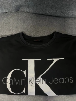 Svart sweatshirt Calvin Klein Jeans - Svart sweatshirt från Calvin Klein Jeans med stort vitt CK-tryck och texten Calvin Klein Jeans på bröstet..