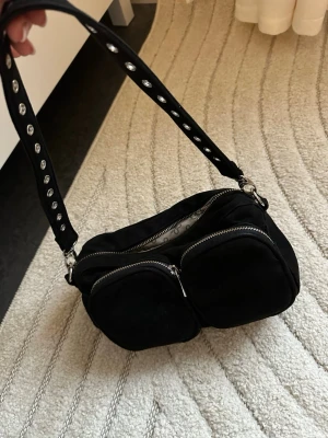 Svart axelväska med nitar och dragkedjor - Svart liten nunoo väska i mocka och massa fickor❤️sjukt fin och en riktigt favorit under många år🥹🥹köpt för 2400kr. Långt band och kort band följer med!