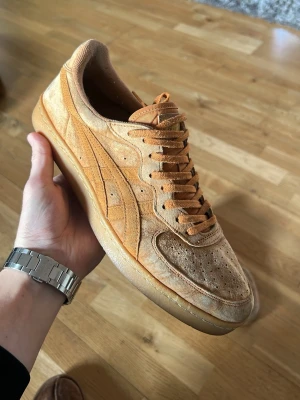 Beige/orange sneakers från Onitsuka Tiger - Säljer ett par snygga beige sneakers från Onitsuka Tiger i mocka. Skorna har klassisk snörning, perforerade detaljer på tån och den ikoniska Onitsuka-loggan på sidan. Perfekta för dig som gillar retrostil och vill ha något unikt till din outfit.