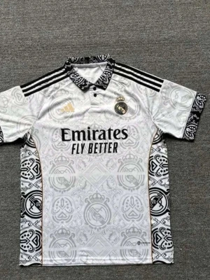 Real Madrid matchtröja mönstrad vit - Säljer en vit Real Madrid matchtröja från Adidas med svart och guldmönster, klubbmärke på bröstet och 'Emirates Fly Better' tryck. Tröjan har svarta ränder påaxlarna, mönstrad krage och ärmslut samt detaljer i guld. Perfekt för fotbollsfans! Helt ny 