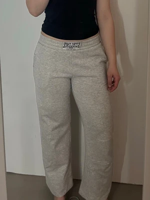 Grå mjukisbyxor från Sublime - Gråa mjukisbyxor från Sublime med bred resår i midjan och logga framtill. Byxorna har raka ben och sidofickor, tillverkade i mjukt bomullsmaterial.