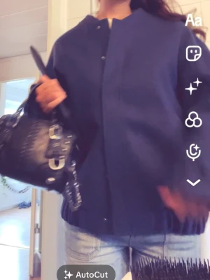 Mörkblå bomberjacka med knappar - Snygg mörkblå bomberjacka med knappar framtill och klassisk ribbad mudd i nederkant. Jackan har en clean look utan synliga loggor eller mönster och passar perfekt till jeans för en avslappnad stil.