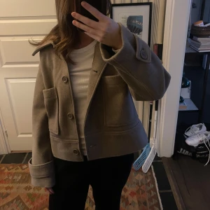 Beige ulljacka med stora fickor - Snygg beige jacka med stora framfickor och krage. 