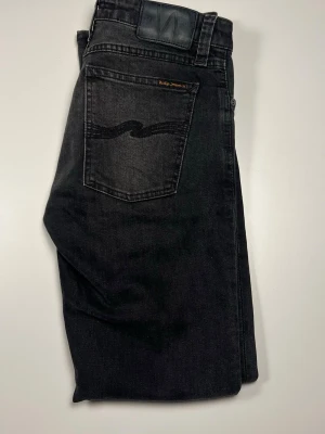 Svarta jeans från Nudie Jeans - Snygga svarta jeans från Nudie Jeans med klassisk femficksdesign och diskret logga på bakfickan. Jeansen har en rak passform och är tillverkade i mjuk bomullsdenim. Perfekta för en avslappnad och stilren look. Kan gå ner i pris vid snabbaffär!!