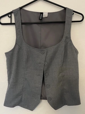Grå väst/linne - Grå lite kortare väst med fyrkantig halsrigning, går att använda som linne.