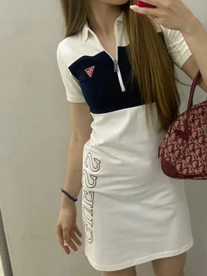 Guess vit och marinblå polo dress  - Polo dress från Guess i vit och marinblå färg med quarter zip  och korta ärmar. Klänningen har en tydlig Guess-logga på bröstet och tryck längs sidan. Tillverkad i mjuk bomull för en bekväm känsla.