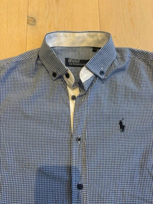Blårutig kortärmad skjorta Polo Ralph Lauren - Kortärmad skjorta från Polo Ralph Lauren i blåvitt rutigt mönster. Klassisk button-down krage och broderad logga på bröstet. Tillverkad i bomull, perfekt för en clean och stilren look.