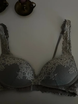 Grå-bh från Intimissimi - Säljer en grå bh från Intimissimi med vadderade kupor och vacker spetsdetalj över hela bh:n. Axelbanden är dekorerade med spets och bh:n har hakknäppning bak. Materialet är mjukt och stretchigt för extra komfort.