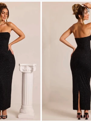 Glittrig svart axelbandslös klänning - Snygg svart axelbandslös klänning från oh polly med glittrigt tyg och slits bak. Klänningen är figurnära och har en elegant bandeau-modell som passar perfekt till speciella tillfällen. 