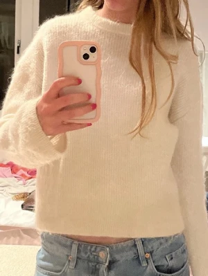 Vit fluffig stickad tröja - Mysig vit stickad tröja med fluffig känsla och rund hals. Tröjan har en rak passform och långa ärmar, perfekt för lager-på-lager. Passar till både jeans och kjol för en chill look.