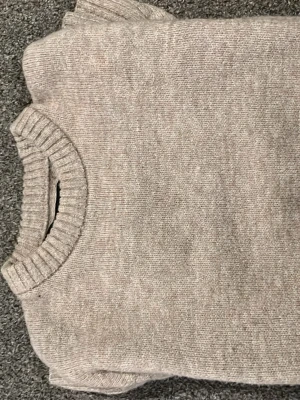 Beige stickad tröja med rund hals - Mysig beige stickad tröja med rund halsringning och ribbade muddar. Perfekt för lager-på-lager och enkel att matcha med olika outfits. Tröjan har en klassisk och stilren design som passar till många tillfällen.