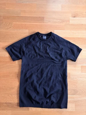 Svart tränings-tshirt från Gymshark - Svart kortärmad t-shirt från Gymshark med diskret mönster i tyget. Perfekt för träning med lätt och ventilerande material som håller dig sval. Snygg passform och stilren design med liten logga på bröstet.