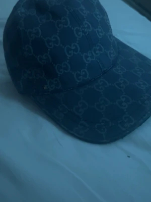 Mörkblå keps med monogram - Snygg mörkblå keps med monogram över hela kepsen. Justerbar rem baktill för perfekt passform. Tillverkad i canvasmaterial som ger en exklusiv känsla och stilren look.