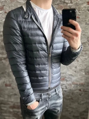 Herno dunjacka  - Snygg mörkblå dunjacka från Herno med quiltad design och dragkedja framtill. Jackan har en smal passform och ståkrage med diskreta detaljer vid kragen. Perfekt för kyliga dagar och enkel att matcha med olika outfits. Storlek 46/S, passar er runt 170-175, modell=185cm