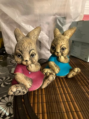 Kaninformade sparbössor i keramik - Två söta sparbössor i form av kaniner, en med rosa klänning och en med blå klänning. Tillverkade i keramik med naturtrogen färg och detaljerat ansikte. Perfekt som dekoration eller för att spara mynt. Myntinkast på baksidan av huvudet.