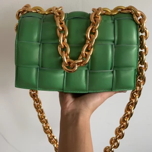 Grön axelväska från Bottega Veneta - Snygg grön axelväska med inspiration av  Bottega Veneta med quiltad design och en rejäl guldkedja som axelrem. Väskan har en stilren look och är perfekt för att ge din outfit en färgklick. Den är tillverkad i skinn och har en elegant stängning framtill. Liten skada på framsidan!!