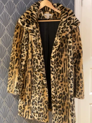 Leopardmönstrad pälsjacka från H&M - Snygg leopardmönstrad pälsjacka från H&M med bred krage och normal passform. Jackan har långa ärmar och är gjord i mjuk fuskpäls som ger en lyxig känsla. Perfekt för dig som vill sticka ut och hålla dig varm under höst och vinter.