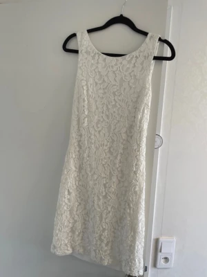 Vit klänning - Snygg vit klänning i spets med ärmlös design och v-ringad rygg. Klänningen har en figurnära passform.  Använd endast en gång. Köpt på bubbleroom i storlek 36.