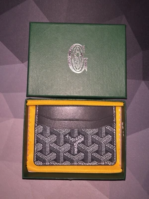 Svart Goy4rd plånbok - Snygg svart plånbok från Goy4rd med ikoniskt vitt och grått mönster. Plånboken har flera kortfack och gula detaljer på insidan. Tillverkad i exklusivt skinn och levereras i original grön ask.