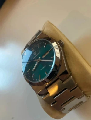 Poedagar Herrklocka Quartz 41mm rostfritt stål - Stilren klocka från Poedagar med grön urtavla och dag/datumvisning. Armbandet är i silverfärgat rostfritt stål med klassisk länkdesign. Quartz-urverk och rund boett i metall. Perfekt accessoar för dig som gillar modern och clean stil.