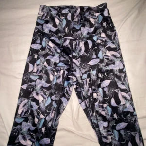 Blommiga högmidjade leggings - Snygga leggings med blommigt mönster i lila, blått och svart. Hög midja och tight passform, perfekta för träning eller chill. Materialet är stretchigt och mjukt för maximal komfort❤️