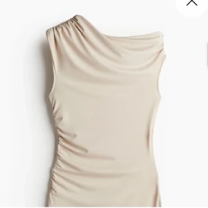 Beige one shoulder klänning H&M - Snygg beige kortklänning från H&M Divided i storlek XS. Klänningen har one shoulder-design med draperad axel och lätt rynkning längs sidan för en cool siluett. Tillverkad i mjukt och stretchigt syntetmaterial som sitter skönt och följer kroppen.