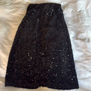 Svart paljettkjol från Vila XS - Svart kjol från Vila i storlek XS, täckt med glittriga paljetter som ger en riktigt festlig vibe. Kjolen har en rak form och en slits bak för extra rörelsefrihet. Resår i midjan för skön passform. Perfekt för dig som vill sticka ut.