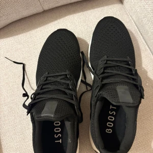 Adidas Ultraboost svarta sneakers - Svarta Adidas Ultraboost sneakers med stickad ovandel och klassiska tre ränder på sidan. Skorna har snörning och en vit Boost-plattformssula som ger grym komfort. Perfekta för dig som gillar stilrena och sportiga sneakers med modern känsla. Helt oanvända och jag kan tänka mig gå ned i pris vid snabb affär.
