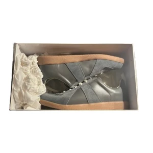 Maison Margiela Gats grå sneakers - Maison Margiela gats sneakers i grått med beige snörning och gummisula. Ovandelen är en mix av mocka och skinn, med klassisk rund tå och platt sula. Snygg retrostil med diskreta detaljer och logotyp på plösen och sulan. Perfekt för dig som gillar minimalistisk design. Får med box och dustbags. Bilderna kan va lite suddiga. Pris kan diskuteras vid snabb affär😁